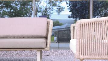 A modern outdoor seating area with a sofa and a wicker chair, both facing a large glass window.