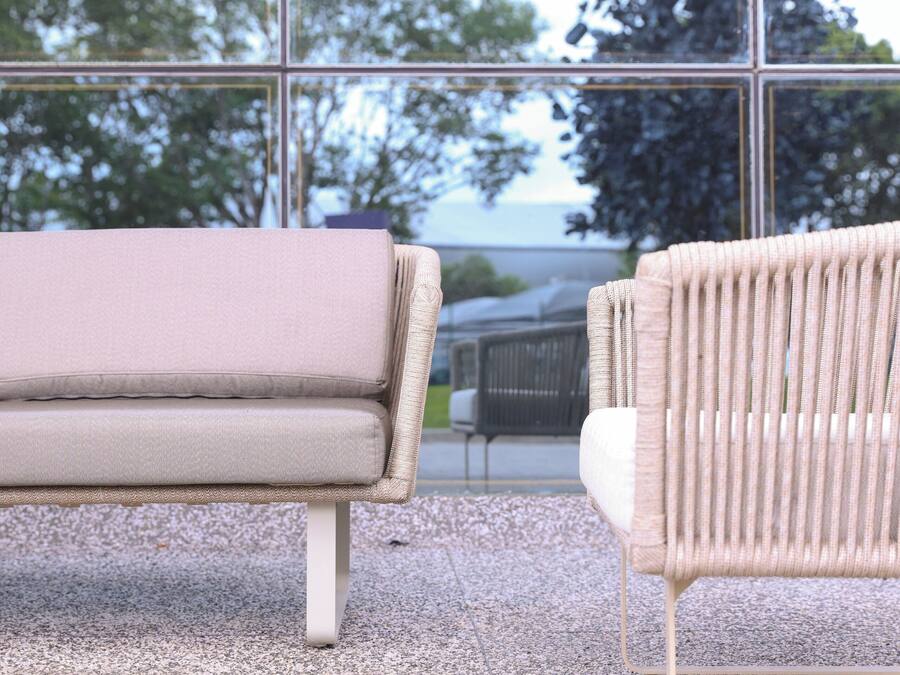 A modern outdoor seating area with a sofa and a wicker chair, both facing a large glass window.