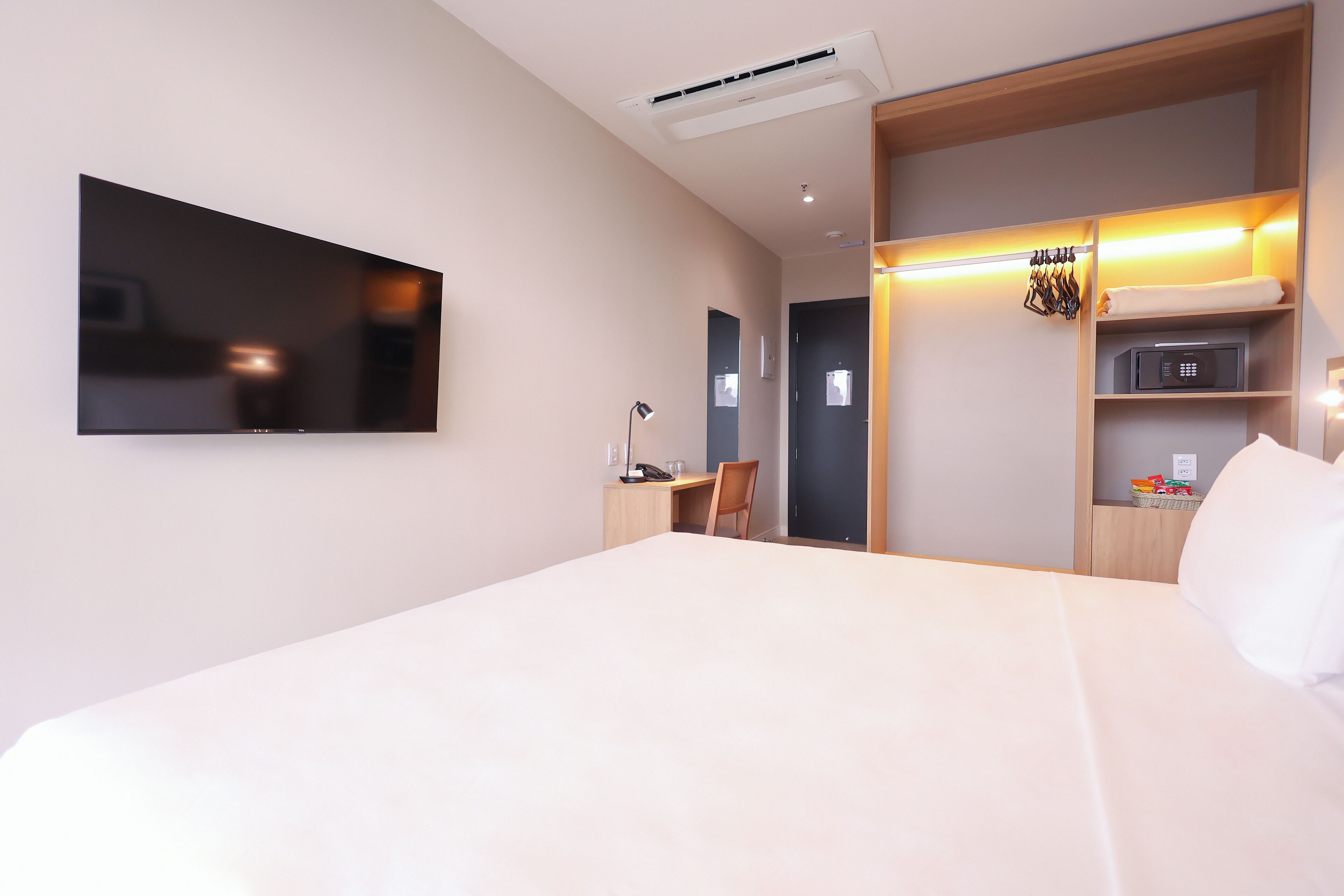A modern hotel room with a large bed, a desk, a chair, a TV, and a wardrobe with a mirror.