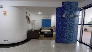 Een moderne lobby met een blauwe mozaïekzuil, een bank en een bijzettafeltje.