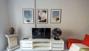 Un salon avec un téléviseur, un ventilateur et trois tableaux encadrés accrochés au mur.