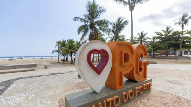 Naamplaatje bij een strandlocatie met 'PG' en 'ANTO' zichtbaar, omringd door palmbomen en een strand.