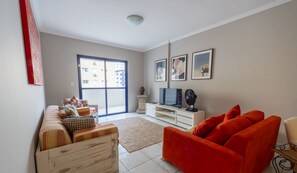 Ein Wohnzimmer mit einer Couch, einem roten Sessel, einem Fernseher und einem großen Fenster.