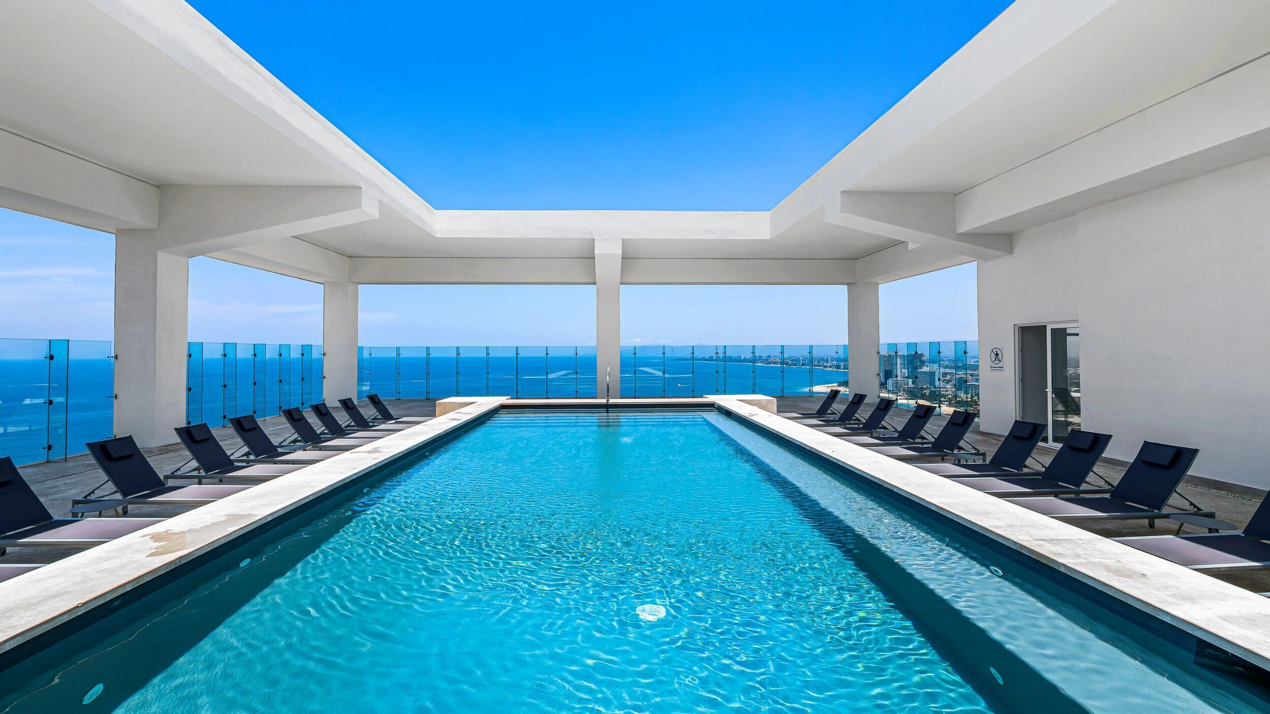 Egy hosszú, téglalap alakú medence, melynek vizében a tiszta, kék szín dominál, és amelyet napozóágyak és üvegkorlát vesznek körül, ahonnan kilátás nyílik az óceánra és a város látképére.