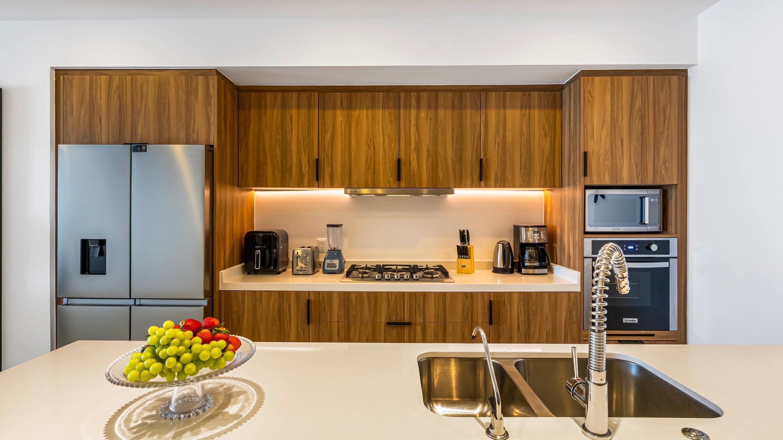 A modern kitchen with wooden cabinets, stainless steel appliances, a built-in oven, and a sink with a unique faucet design.