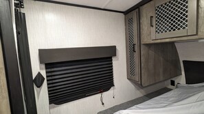 A compact RV interior with a bed, a headboard, and a small kitchenette area. - Delightful RV with AC in Palmdale (Palmdale)
