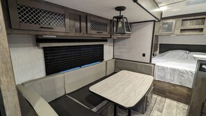 A compact RV interior with a kitchenette, a dining area, and a sleeping berth.