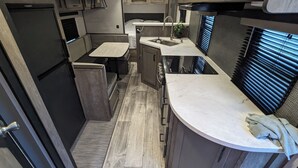 A compact RV kitchen with a sink, stove, and wooden flooring.