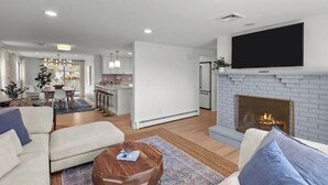 A modern living room with a fireplace, a dining area, and a kitchen. - Eventide: Renovated 5 Bedroom, 3 Baths on Aquidneck Island (Portsmouth)