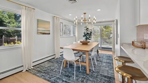 A modern dining area with a wooden table, white chairs, and a black rug. - Eventide: Renovated 5 Bedroom, 3 Baths on Aquidneck Island (Portsmouth)