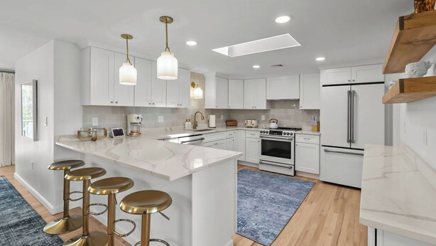A modern kitchen with white cabinetry, a central island with stools, stainless steel appliances, and pendant lighting. - Eventide: Renovated 5 Bedroom, 3 Baths on Aquidneck Island (Portsmouth)