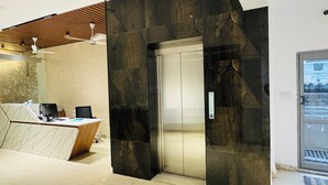 Una moderna zona de recepción con un escritorio de mármol, un elevador con marco negro y una puerta de cristal.