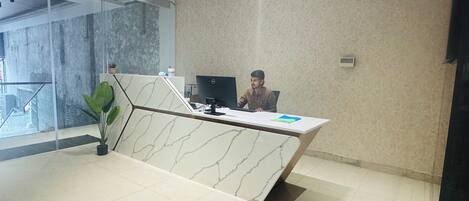 A reception desk with a marble design, a computer, and a plant.