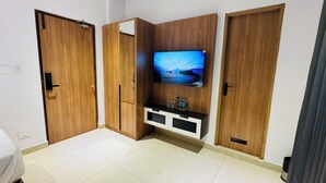 Una habitación de hotel con un televisor fijado a una pared de madera, una pequeña mesita con algunas botellas y una cama con cubrecama blanco.