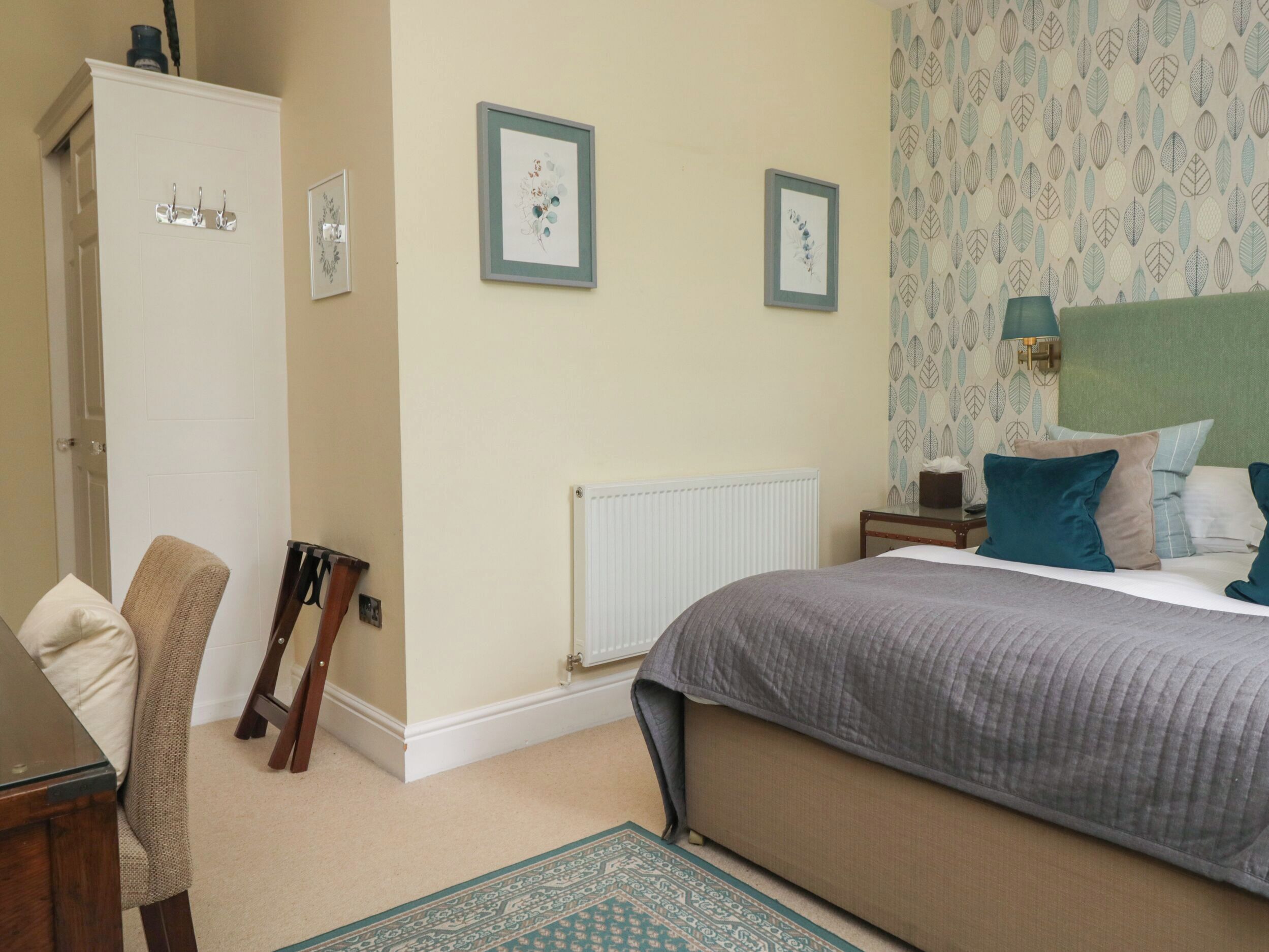 A bedroom with a bed, a wardrobe, a chair, a radiator, and framed pictures on the wall.