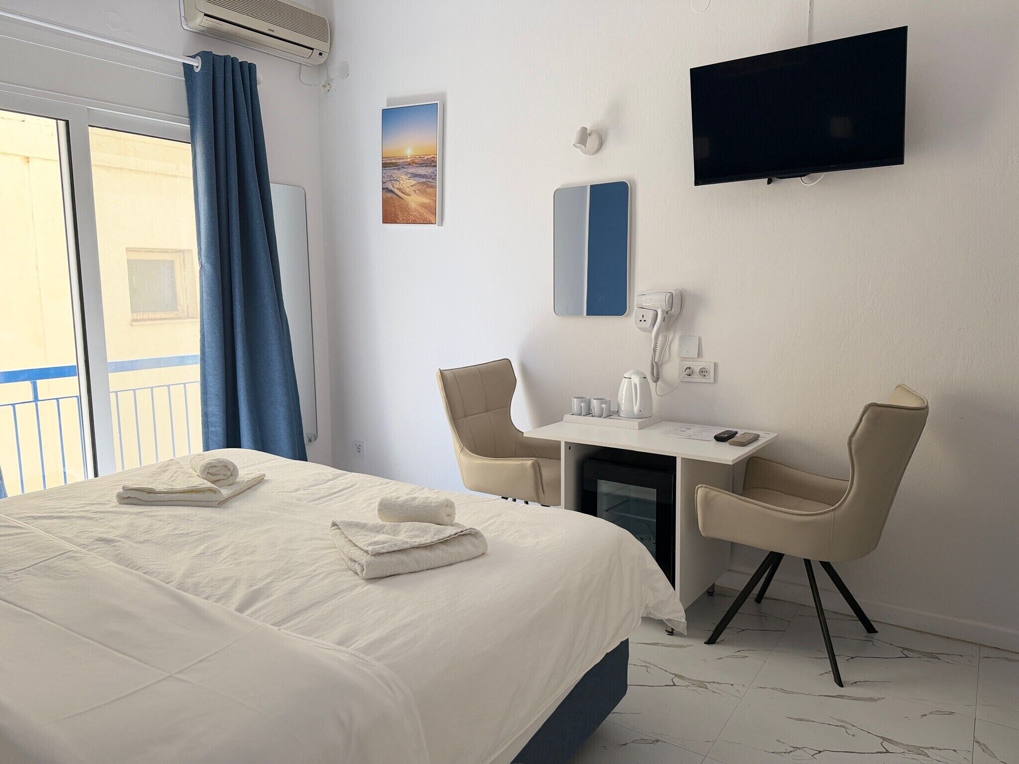 A hotel room with a bed, a desk, two chairs, a TV, a phone, and a window with curtains.