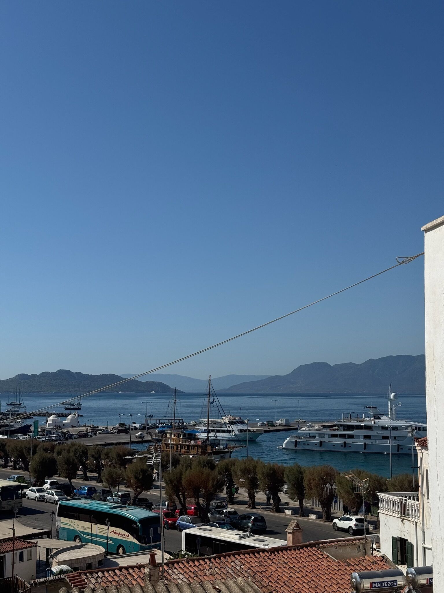 Un puerto deportivo costero con barcos, cielo despejado y montañas a lo lejos.