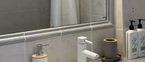Une salle de bain avec un lavabo blanc, un miroir et un rideau de douche.