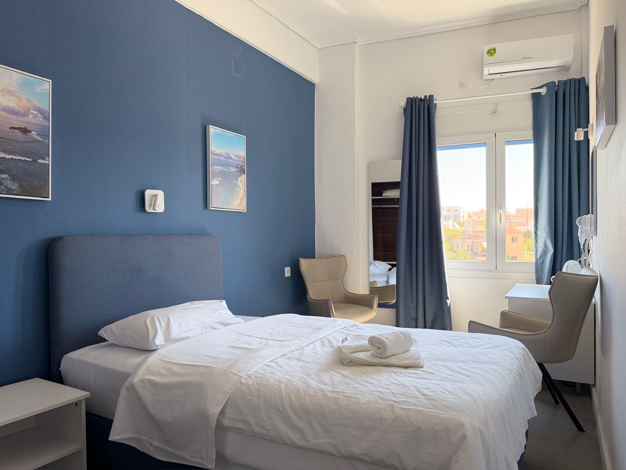 Habitación de hotel con cama, escritorio, silla, armario y ventana con cortinas.
