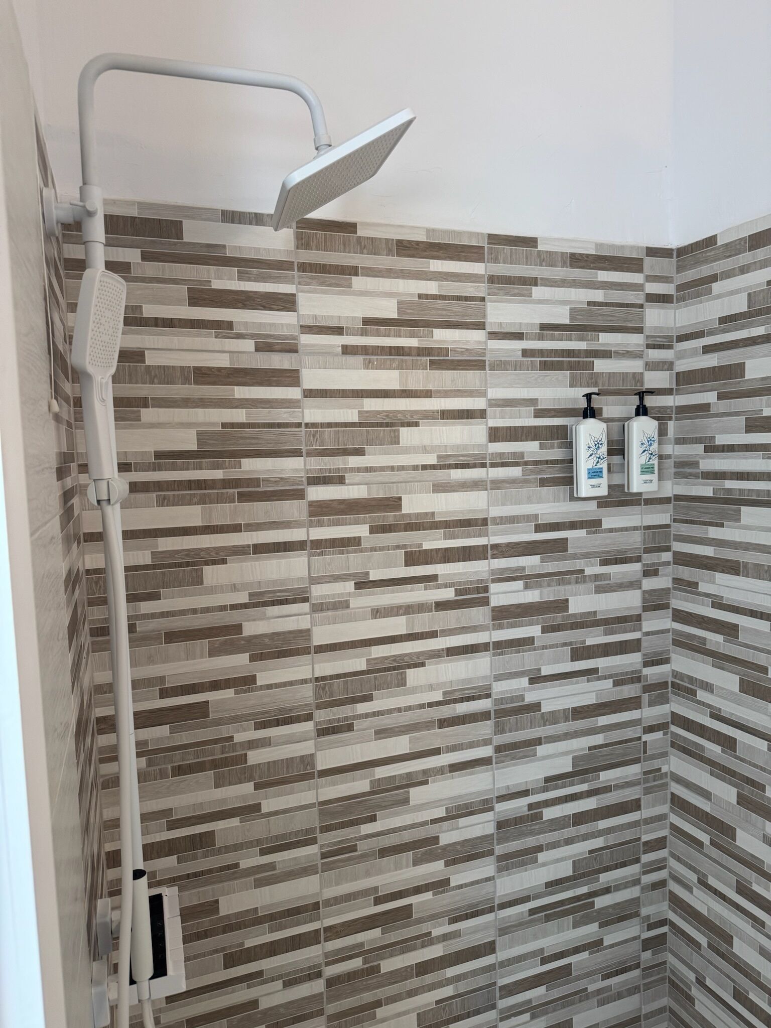 A shower with a rain showerhead and a tiled wall with a wood-like pattern.