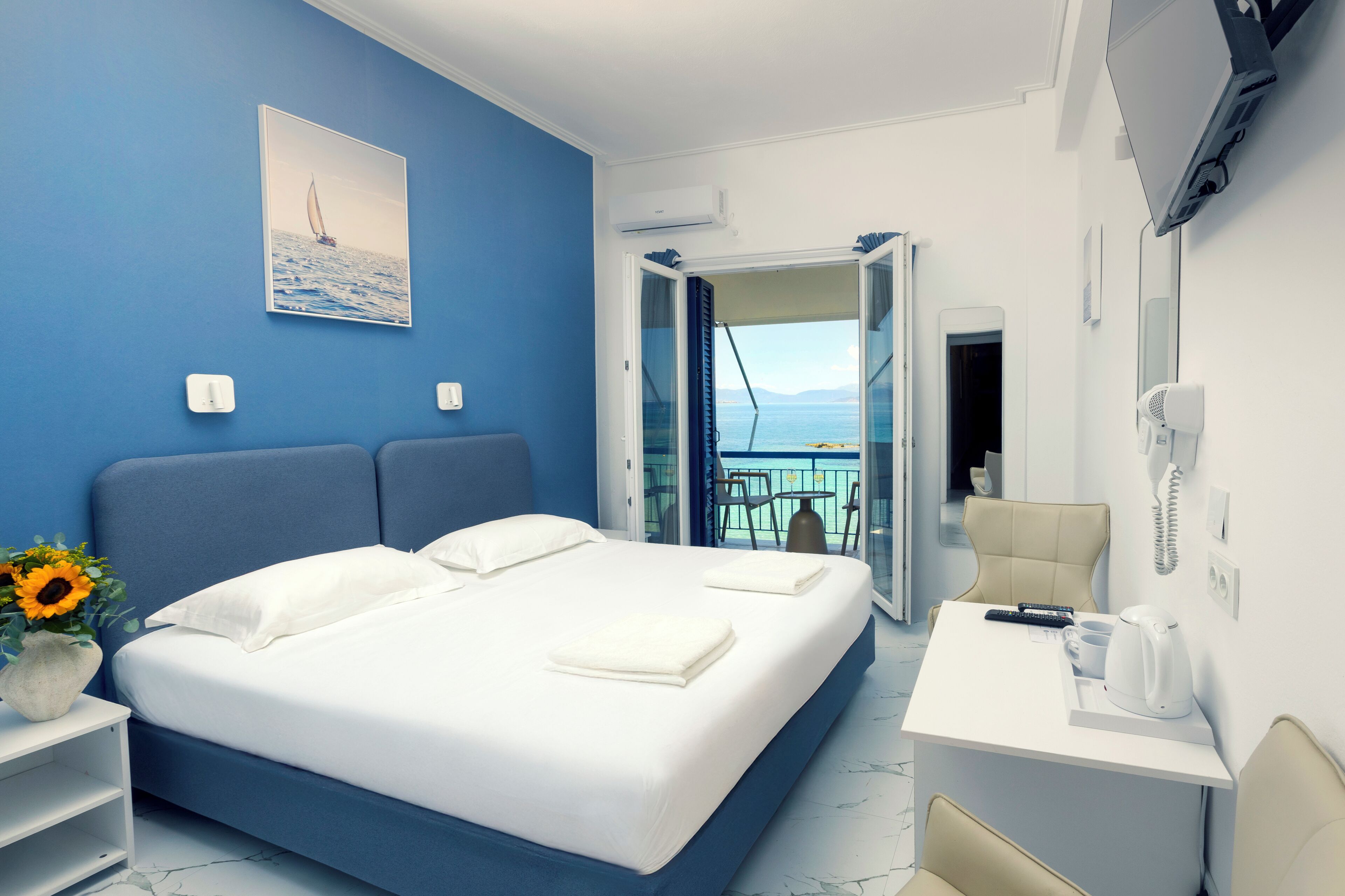 Ein Hotelzimmer mit Bett, Schreibtisch, Stuhl, Blumenvase und Meerblick.