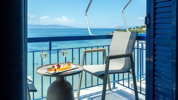 Un balcón con mesa lista para comer, una silla y vista al mar.