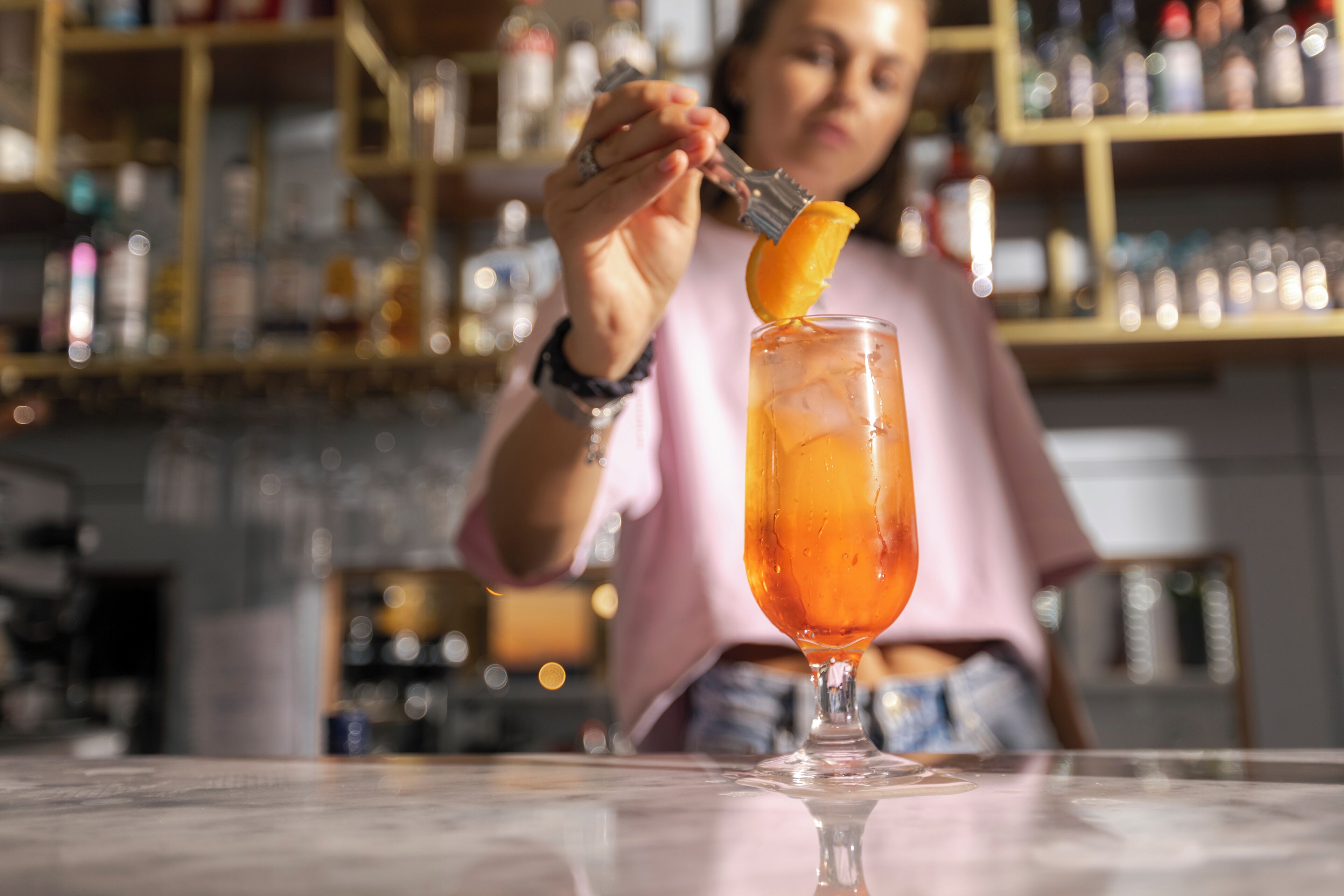 Eine Person an der Bar mit einem Getränk im hohen Glas, eine Bar mit Regalen voller Flaschen und einem unscharfen Hintergrund.