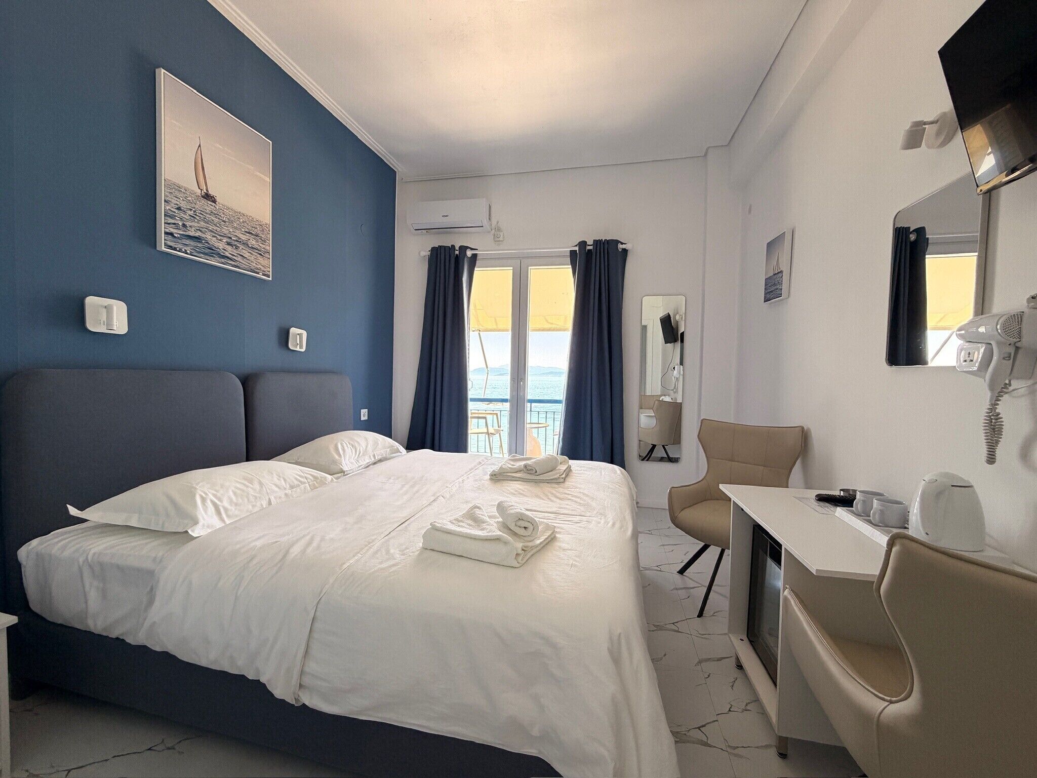 Quarto de hotel com cama, escrivaninha, cadeira, espelho e vista para o mar.