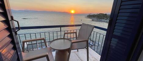 Un balcón con mesa y sillas, con vista a la puesta de sol sobre el mar.