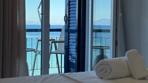 Habitación de hotel con cama, ventana con vista al mar y balcón con silla y mesa.