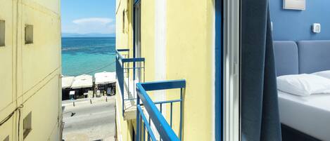 A balcony with a view of the sea, a bed with white bedding, and a blue railing.
