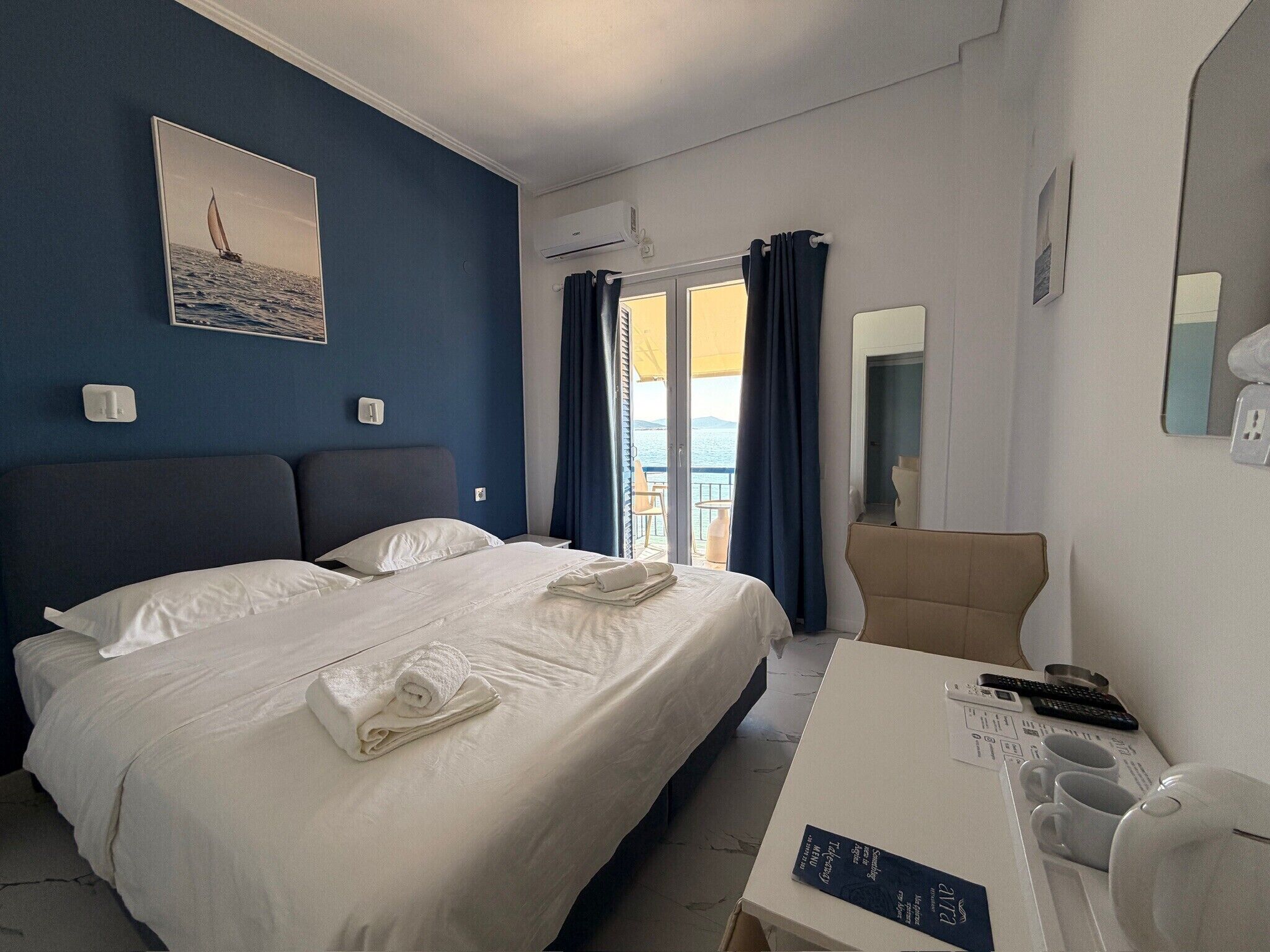 A hotel room with a bed, a desk with a computer, a chair, and a view of the sea.