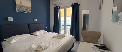 A hotel room with a bed, a desk with a computer, a chair, and a view of the sea.