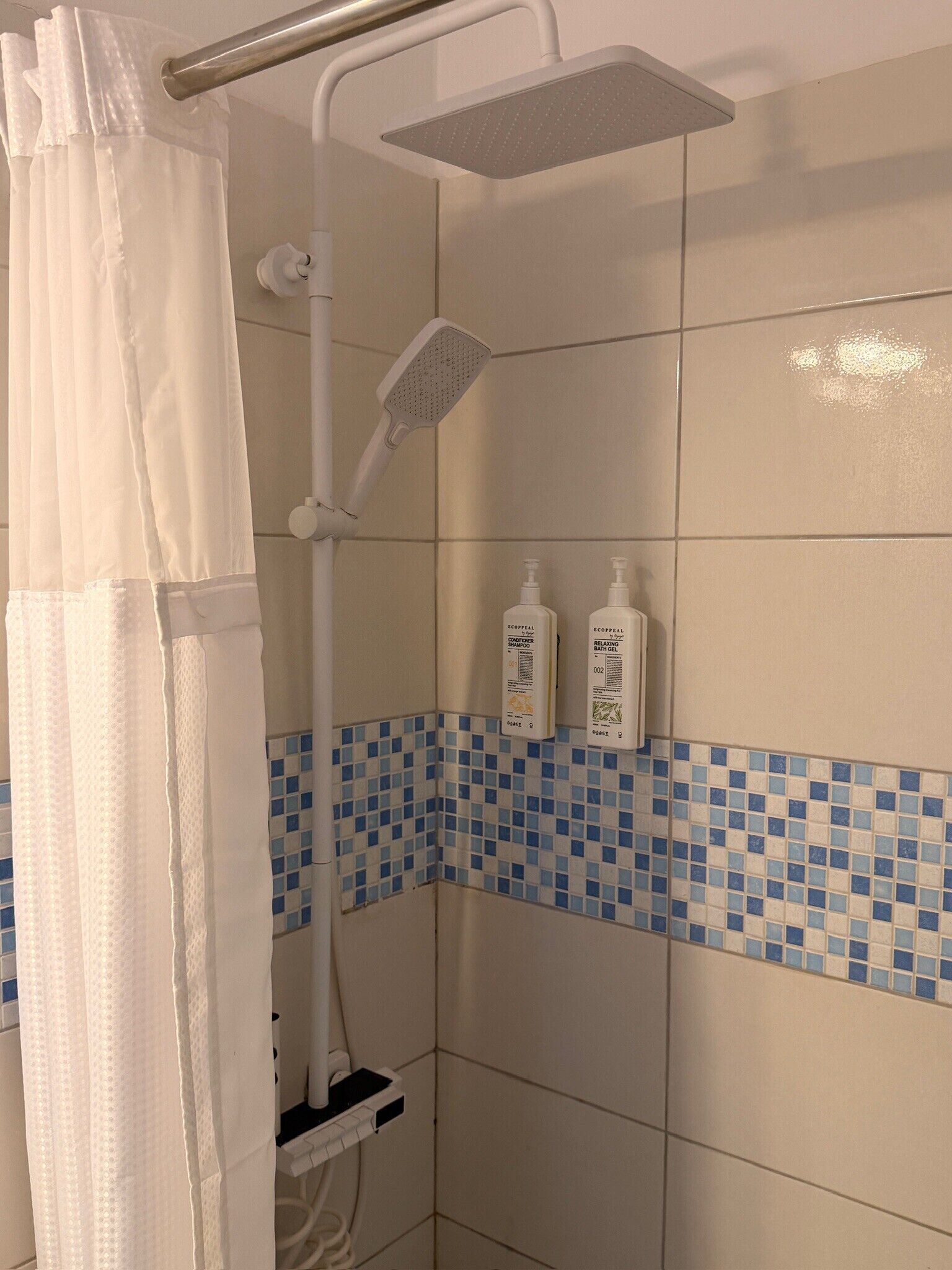 Doccia con soffione a mano, tenda bianca e due flaconi di shampoo a parete.