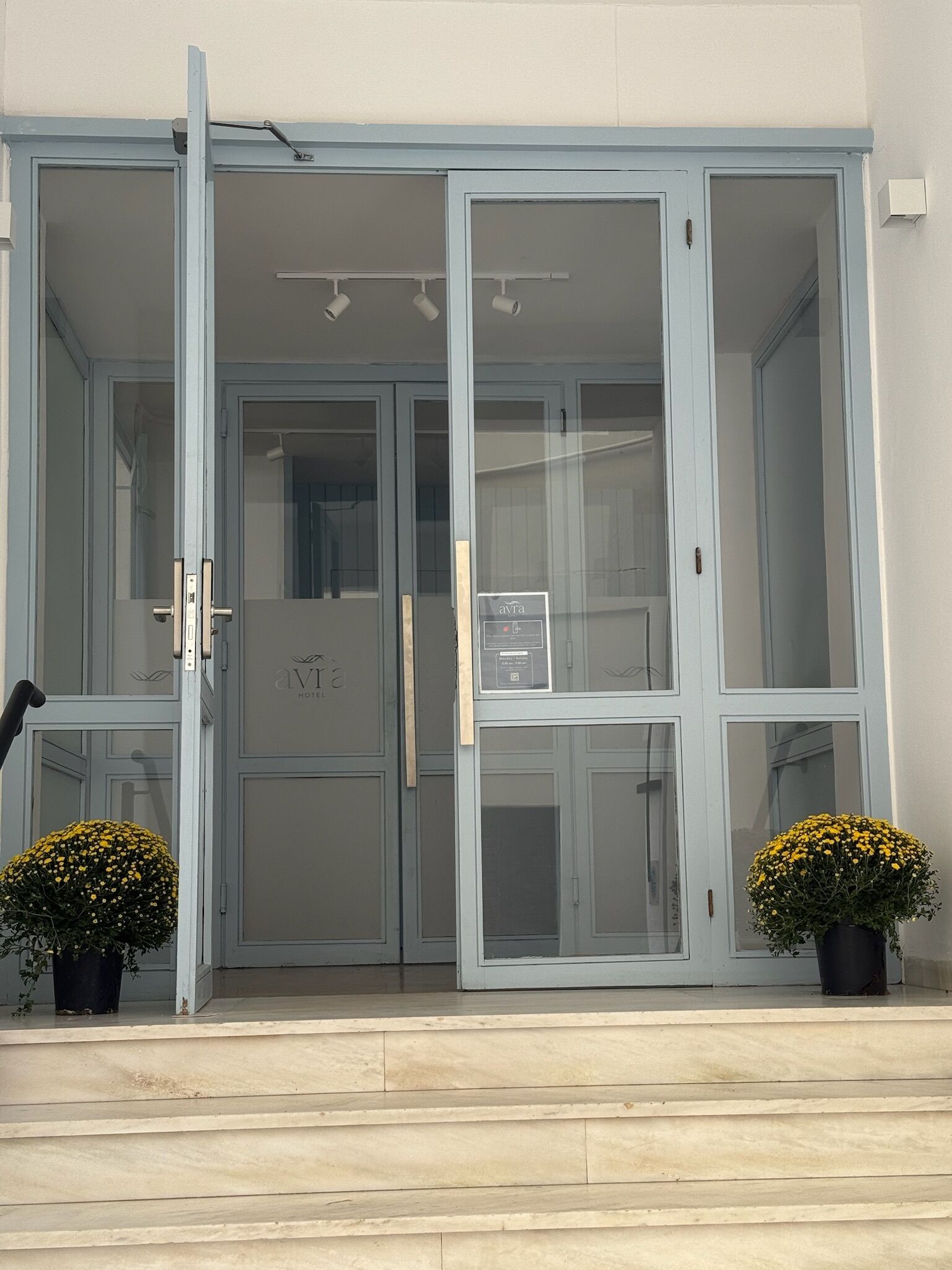 A building entrance with a glass door, a signboard, and two potted plants.