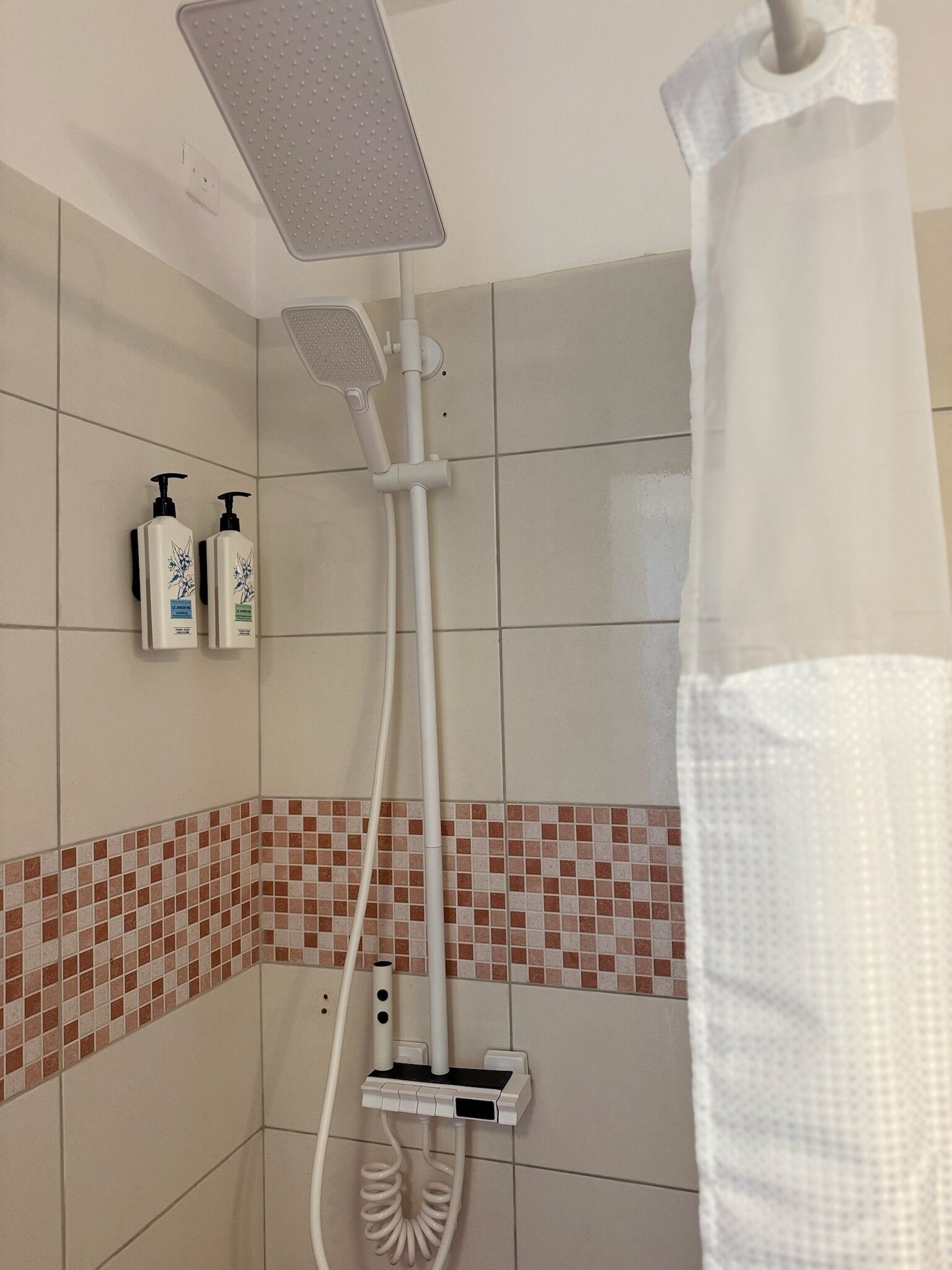 Zona de ducha con cabezal de ducha manual, panel de control en la pared y dos botellas de champú.
