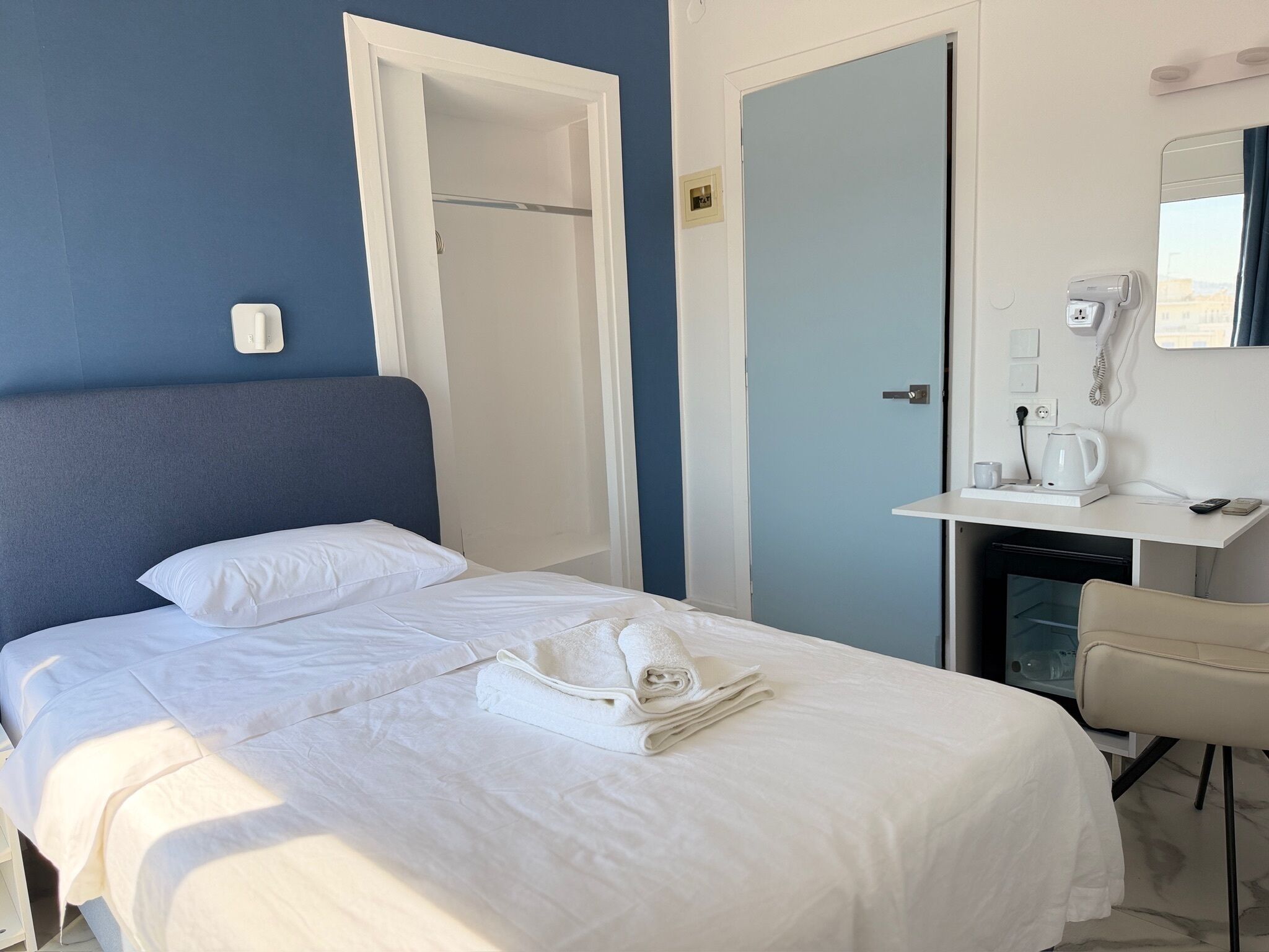 Une chambre d’hôtel avec un lit, un bureau doté d’un téléphone et d’une bouilloire, et une porte.