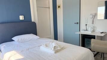 Une chambre d’hôtel avec un lit, un bureau doté d’un téléphone et d’une bouilloire, et une porte.