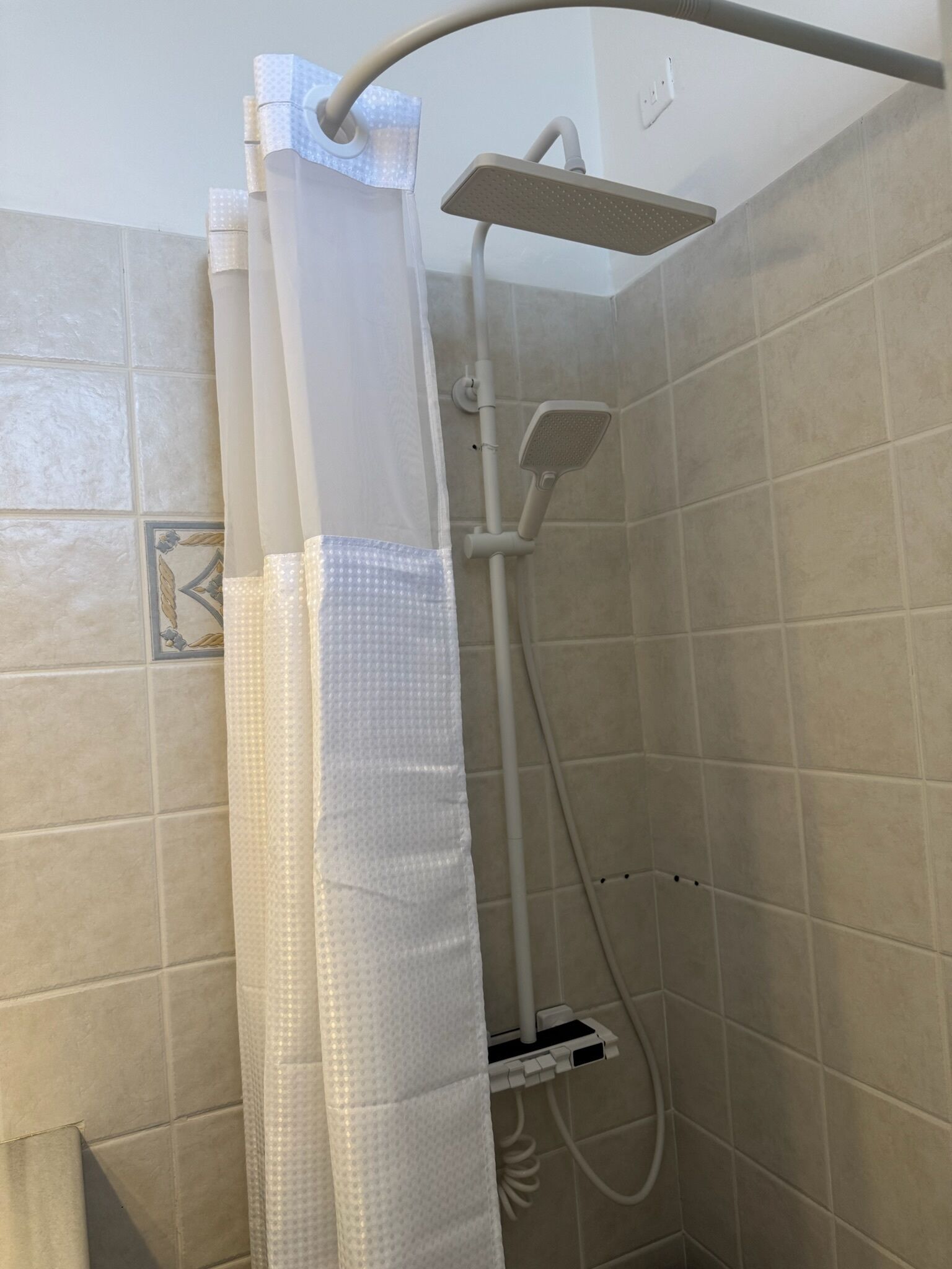 Une douche avec un pommeau de douche blanc et un rideau de douche blanc.