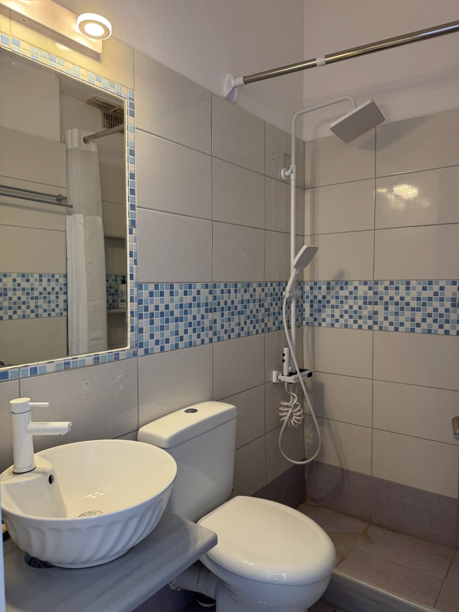 Une salle de bain avec un lavabo, des toilettes et une douche, le tout de couleur blanche.