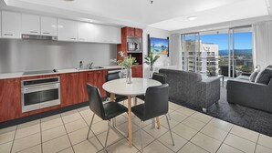 A modern kitchen with white cabinets, a dining area with a round table and chairs, and a balcony with a sofa and a view of the city.