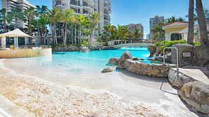 A resort pool area with clear water, palm trees, and a stone bridge.