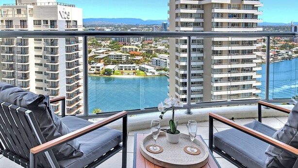 A balcony with two chairs and a small table, overlooking a marina and buildings.