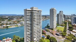 A high-rise building with a 'Waterways' sign, surrounded by other buildings, a river, and a clear sky.