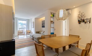 Uma sala de estar moderna com área de jantar, sofá, televisão e uma janela grande.