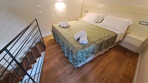 A neatly made bed with a green bedspread and white pillows, a wooden floor, and a white wall with a light switch. - Cozy B&B room on two levels ideal for 2 or 3 people (Belmonte Calabro)