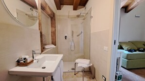 A bathroom with a sink, mirror, shower, and a green couch in the adjacent room. - Cozy B&B room on two levels ideal for 2 or 3 people (Belmonte Calabro)