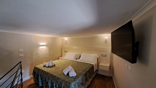 A hotel room with a bed, a TV mounted on the wall, and a small bedside table. - Cozy B&B room on two levels ideal for 2 or 3 people (Belmonte Calabro)