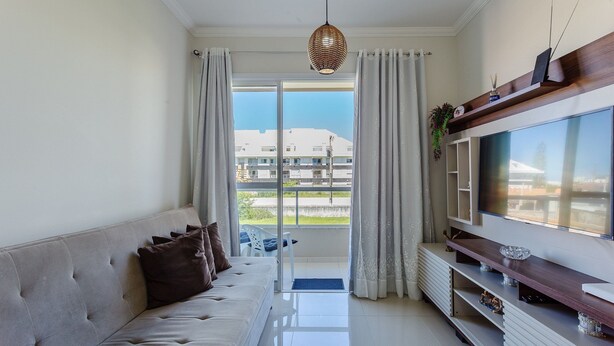 A modern living room with a sofa, TV, and a balcony with curtains. - Cozy Apartment 5 Mi From the Beach, Floripa Ece104 (Florianópolis)
