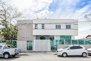 Un bâtiment moderne avec une entrée sécurisée par un portail, une voiture garée devant et un camion garé sur le côté gauche.